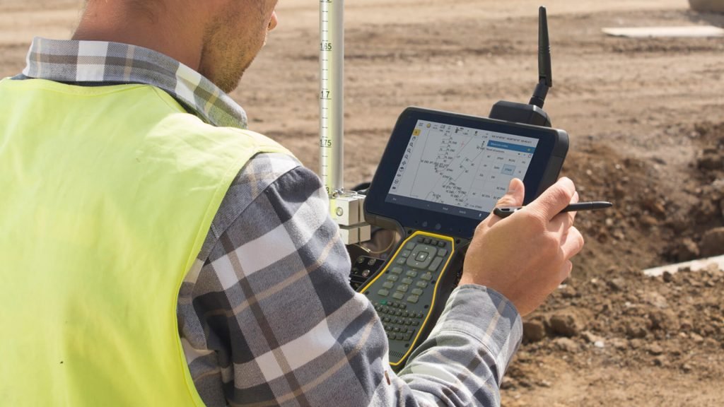 Surveyor using Machine Control Systems on a construction site, capturing and managing grading data with a field controller for improved earthmoving accuracy.