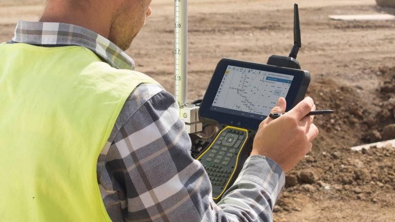 Surveyor using Machine Control Systems on a construction site, capturing and managing grading data with a field controller for improved earthmoving accuracy.