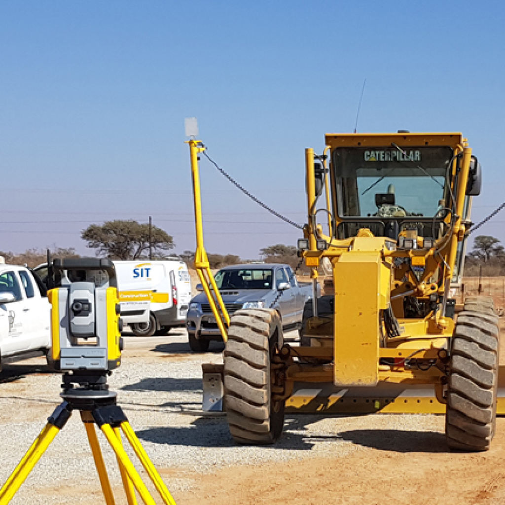 Motor grader on a road construction site using Trimble Earthworks technology for precise grading and excavation.